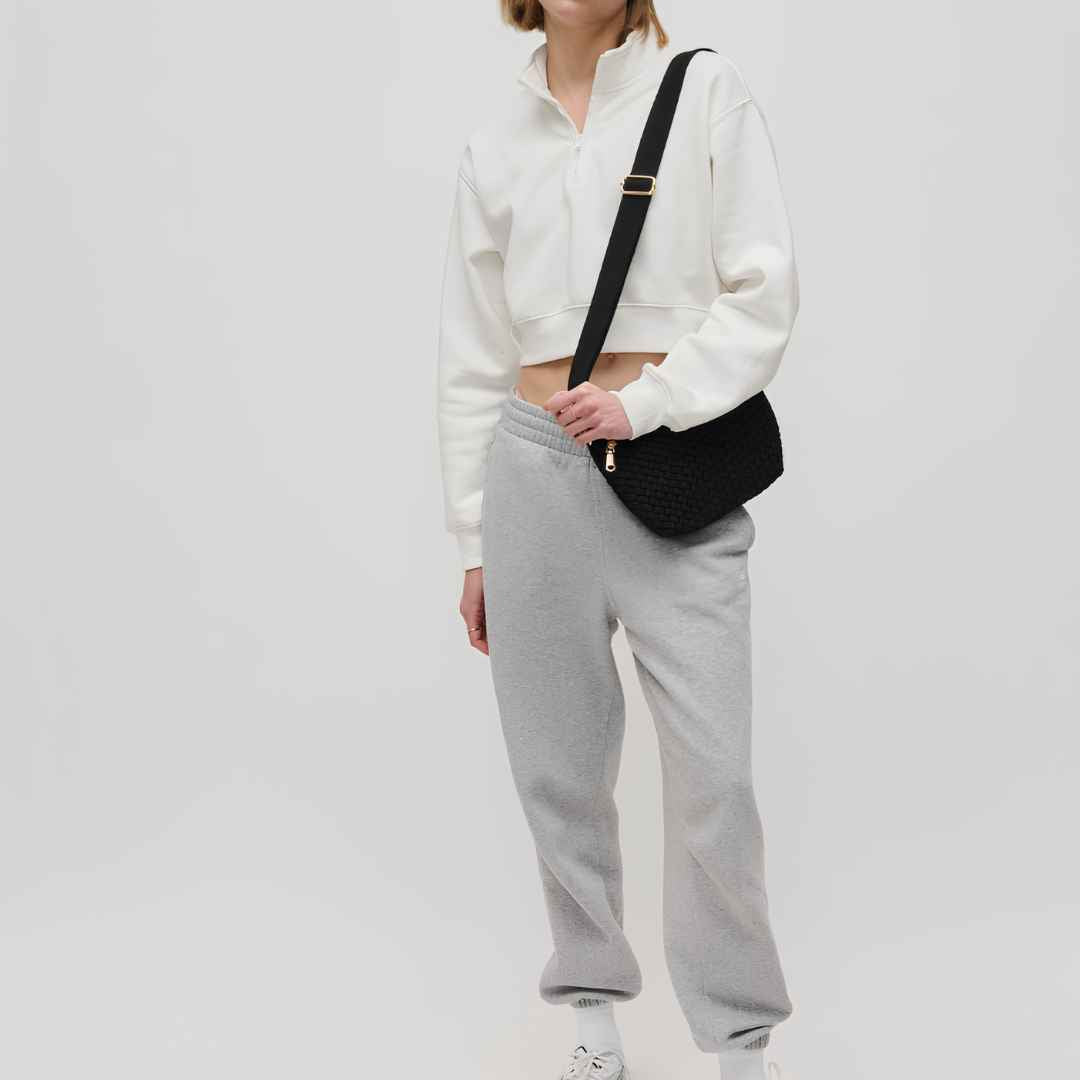 A model carrying a black vegan shoulder bag with a gold buckle.