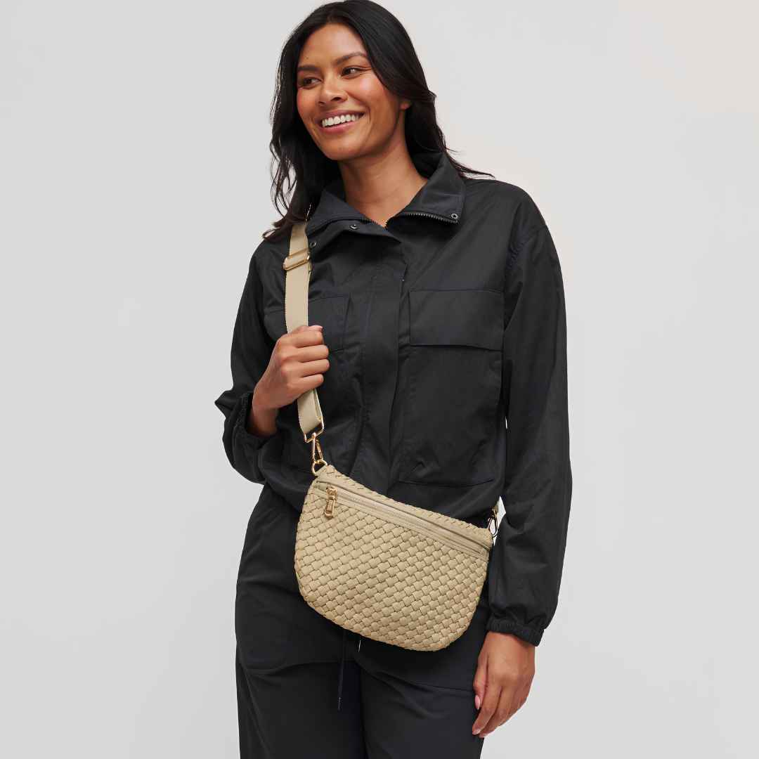 A woman wearing  a beige woven vegan crossbody bag with a matching strap against a light gray studio background.
