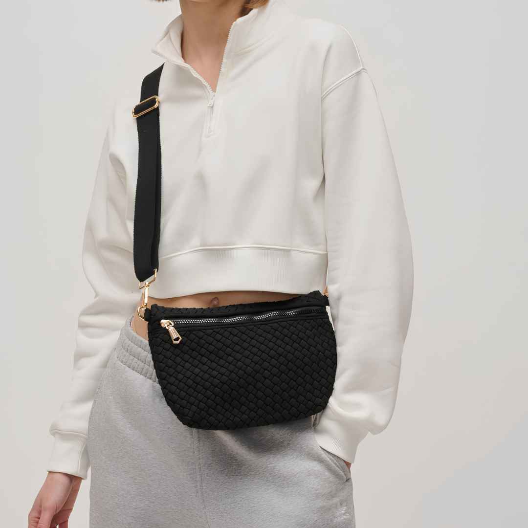A person wearing a black vegan woven crossbody bag with gold-tone hardware and a black strap