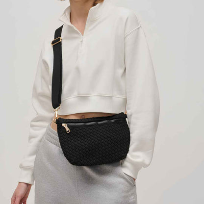 A person wearing a black vegan woven crossbody bag with gold-tone hardware and a black strap